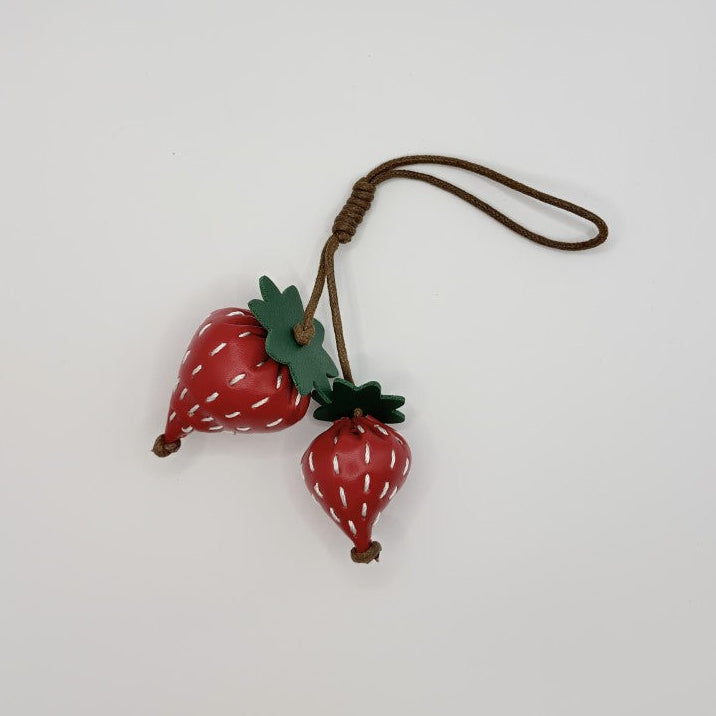Two red vegan leather strawberry bag charms with green leaves and cord loop