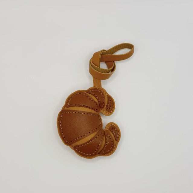 A small brown leather keychain charm shaped like a stylized crescent moon or folded leaf, with a loop at the top, photographed on a plain white background.