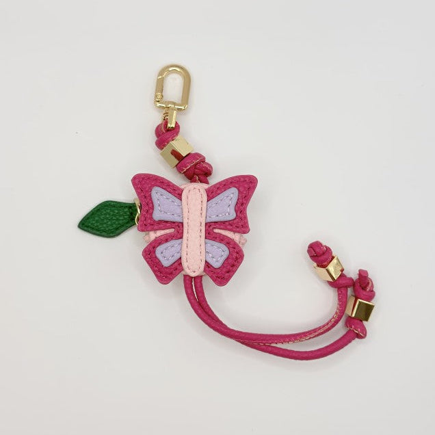 A butterfly-shaped keychain charm featuring pink and light purple wings, a green leaf, and a gold-tone lobster clasp on a white background.